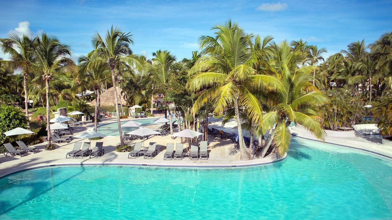 Catalonia Punta Cana Exterior foto The photo shows a serene resort pool area surrounded by lush palm trees. The water is a clear, inviting turquoise, and there are lounge chairs arranged around the pool. Sun umbrellas provide shade for those relaxing by the water. In the background, t