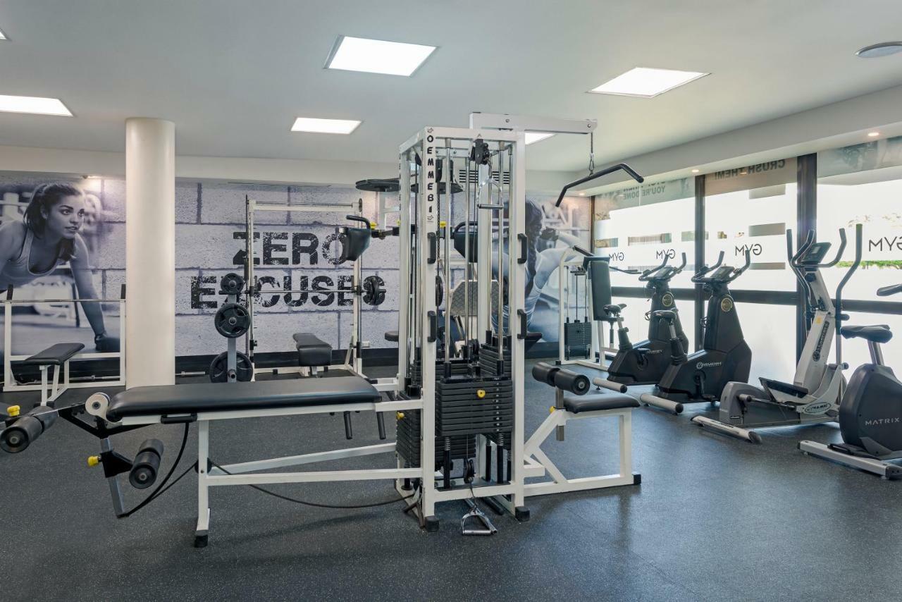 Catalonia Punta Cana Exterior foto The photo showcases a gym interior featuring various exercise equipment. In the center, there is a multi-functional weight machine. Surrounding it, there are several upright exercise bikes lined up against a wall with large windows, allowing natural 